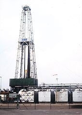 Drilling rig with pipe string sections, next to it container for the drilling fluid