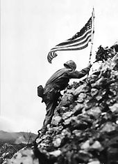 Подполковник Ричард П. Росс, командир 1-го батальона 1-й морской пехоты, смело стреляет снайперским огнем, чтобы 30 мая расставить цвета дивизии по замку Шури. Этот флаг был сначала поднят над мысом Глостер, а затем над Пелелью.