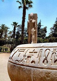 Hieroglyfy na kameni; za nimi socha Ramsese II.
