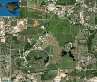 Uma vista de satélite do Fermilab. As duas estruturas circulares são o Anel Injetor Principal (pequeno) e o Tevatron (grande).