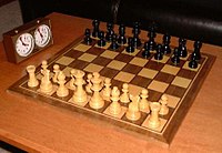 Stauntonin shakkinappulat shakkilaudalla ja shakkikello.  