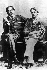 Due uomini in giacca e cravatta siedono su una panchina con le gambe incrociate. Wilde e il suo amante, Lord Alfred Douglas, nel 1893.