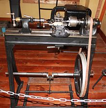 The lathe is driven by a foot rocker, chain and flat belt