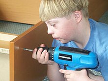 Un bambino con la sindrome di Down che costruisce una libreria (in questa fotografia il trapano non è in azione)