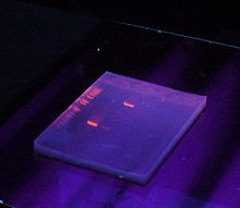 Block av gel som ses under ultraviolett lampa (UV). Banden är rödfärgade.  