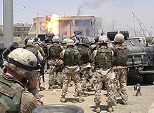 Soldaten van de 101ste Airborne Division en U.S. Special Operations (Task Force 20) kijken toe hoe een TOW-raket de zijkant raakt van een huis dat bewoond werd door Uday en Qusay Hussein in Mosul, op 22 juli 2003