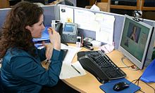 Uma pessoa surda no trabalho comunicando-se com uma pessoa auditiva utilizando um Serviço de Relé de Vídeo. Ela usa a linguagem de sinais, que o operador traduz em voz alta para a pessoa auditiva.