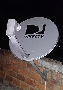 Standardní satelitní anténa DirecTV s duálním LNB na cihlové zdi. Zobrazená parabola používá staré logo zmíněné pobočky AT&T.  