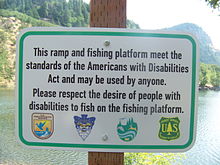 A ADA estabelece padrões para a construção de instalações públicas acessíveis. Exibido é um sinal indicando uma plataforma de pesca acessível no Lago Drano, Washington.