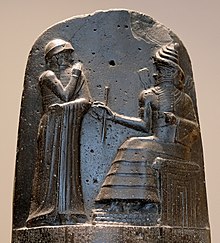 Hammurabi (în picioare), reprezentat ca primind însemnele regale de la Shamash (sau, posibil, de la Marduk). Hammurabi își ține mâinile deasupra gurii în semn de rugăciune (relief pe partea superioară a stelei codului de legi al lui Hammurabi).  