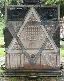 La stella di Davide e il candelabro a sette braccia (menorah) sono simboli degli ebrei e del giudaismo. Il cubo in questa foto si trova al posto di una vecchia sinagoga. È stato fatto per ricordare l'Olocausto.