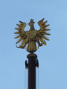 Artistically stylized, entirely gold-coloured figure of the heraldic eagle on a flagpole in front of the parliament