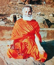 Rāmabhadrācārya mantendo sua mente fixa nas margens do rio Mandakini durante um Payovrata. Ele está na pose de Sukhasana com os dedos dobrados no Mudra do Chin.