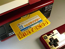 FDS with yellow game disk and game controller. Some letters in the Nintendo lettering on the disk are recessed as a copy protection measure.