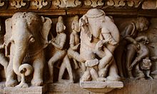 Lakshmana temple in the temple district of Khajuraho - elephant frieze with erotic scene. The right elephant is so irritated by the hustle and bustle (brahmin and girl) at his side that he has thrown one of his attendants (mahut) to the ground with his trunk and threatens to crush him with his raised foot. Whether the scene is merely entertaining or was meant to instruct or warn must remain open.