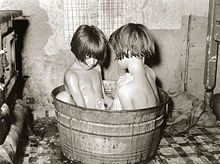 Twee kinderen badend in een kleine metalen badkuip