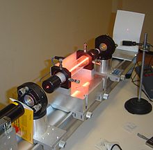 Demonstration laser: In the middle you can see the glow of the gas discharge that excites the laser medium. The laser beam can be seen on the right as a red dot on the white screen.