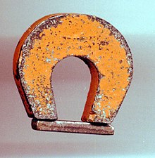 Um "ímã em ferradura" feito de Alnico 5, cerca de 1 pol. de altura. A barra de metal (inferior) é um guardião. Colocada sobre os postes quando o ímã não estava em uso, ela ajudou a preservar a magnetização.