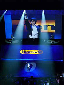 Miyamoto houdt een Wii-afstandsbediening omhoog op de E3 2006  