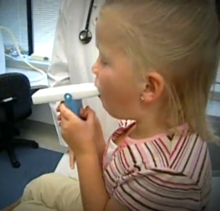 Een kind gebruikt een piekstroommeter (PFM) die meet hoe goed de lucht uit de longen van een persoon stroomt (de peak expiratory flow, of "PEF") wanneer deze uitademt.  