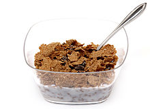 Eine Schale mit Rosinenkleie-Getreide in einer durchsichtigen Plastikschale und fettarmer Milch. Dies ist ein gutes Beispiel für fettarme Lebensmittel.