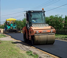 Construction of a road with an asphalt concrete surface using an asphalt concrete paver (at the back of the picture) and a two-wheel smooth roller (at the front of the picture)