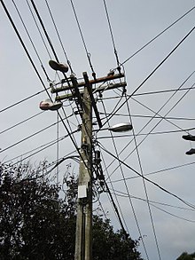 Mast mit Telefon-, Strom- und Kabelfernsehgeräten. Man sieht zwei Paar Schuhe, die an Drähten hängen.