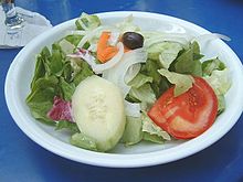 Bord met groene salade, ui, tomaat, komkommer, wortel en een zwarte olijf  
