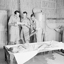 Artimuosiuose Rytuose britų kareivį ištinka šilumos smūgis ir jis vėsinamas vandens purškalu (1943 m.)