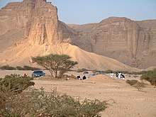 Local family at a picnic in the desert at the foot of the Jebel Tuwaiq, the men at prayer