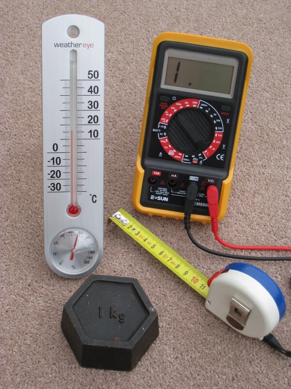Quatre appareils de mesure quotidiens à calibrage métrique : un mètre ruban calibré en centimètres, un thermomètre calibré en degrés Celsius, un poids en kilogrammes et un multimètre électrique qui mesure les volts, les ampères et les ohms.