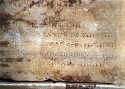 Fotografia oryginalnego kamienia w Delfach zawierającego drugi z dwóch hymnów do Apolla. Notacja muzyczna to linia okazjonalnych symboli ponad główną, nieprzerwaną linią greckiego liternictwa.