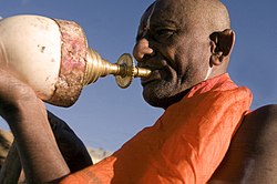 Un sacerdote indù che soffia in uno strombo durante una puja