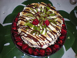 Een pavlova met aardbeien, bananen, kiwi's en room.