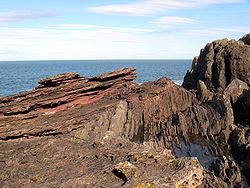 Siccar Point: eroderade och svagt sluttande lager av gammal röd sandsten från Devon över konglomeratskikt och äldre vertikalt lagrade gråwackegrunder från Silur.  