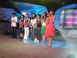 Seis finalistas durante una prueba de la ronda nacional de 2005 en Changsha, Hunan. De izquierda a derecha: el presentador Li Xiang, los concursantes Lin Shuang, She Man Ni, Yi Hui, Jane Zhang (Zhang Liang Ying), Guo Hui Min, Li Na y el presentador Wang Han.