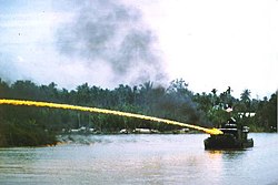 Rivierboot van de Amerikaanse Brownwater Navy die een brandende mix van napalm van een vlammenwerper in Vietnam schiet.