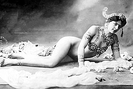 Mata Hari. Il segmento più celebrato del suo atto scenico era il progressivo spogliarsi dei vestiti fino ad indossare solo un reggiseno ingioiellato e alcuni ornamenti sulle braccia e sulla testa.