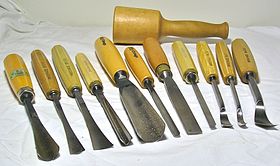 Eine Auswahl an Handwerkzeugen für die Holzschnitzerei: 3 Fischschwanzmeißel, ein V-förmiges Werkzeug, 4 gerade Meißel, 3 Löffelmeißel und ein Schnitzerschlegel