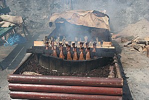 Ράβδοι μπακαλιάρου σε σπιτικό καπνιστήριο. Στον πυθμένα σιγοκαίει ξύλο από σκληρό ξύλο. Η σακούλα στο πίσω μέρος χρησιμοποιείται για να σκεπάζει τα ράφια ενώ καπνίζονται.