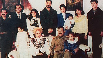 A família Saddam em meados da década de 1980. Uday está de pé na fila do meio da fila de trás com o casaco preto