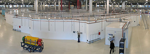 Interiér australského synchrotronu. Dominantou snímku je skladovací prstenec, na kterém je vpravo vpředu vidět optická diagnostická svazková linka. Uprostřed úložného prstence je urychlovací synchrotron a linac.  
