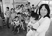 A Vietnamese professor from the Tu Du Hospital for Obstetrics and Gynecology with a group of children, some of whom are severely handicapped. The child in the foreground, for example, has no eyes. The boy on the far left (back) has only one leg.