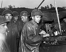 Amerikanske soldater fra 77. division lytter passivt til radiorapporterne om dagen for sejren i Europa den 8. maj 1945.  