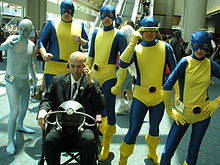 Cosplayers of the original X-Men from 1963 in their blue and gold masked uniforms. From left to right: Iceman, Beast, Professor X (seated), Angel, Cyclops, Marvel Girl.