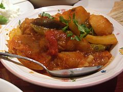 Таджин е ястие, което често се сервира с кускус и зеленчуци по гръцки, запечени с домати и билки.  