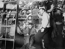 A British sub-lieutenant at the torpedo launch control and a sailor with the book to log launches on an S-class submarine