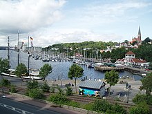 In the city centre, the Hafenspitze, a central place of regular events in Flensburg, marks the beginning of the Flensburg Fjord. In the background, St. Jürgen Church, the Volkspark with the Mürwiker Water Tower, Werftkontor and the silos of Flensburg's industrial port (from right to left, 2011).