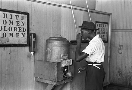 一名男子在 "有色人种"（非裔美国人）的饮水机上喝水；白人的饮水机就在他旁边（1939）。